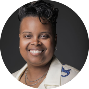 Amber Senter, a black, smiling woman with short hair wears a white collared shirt with blue flowers and alligators on it.