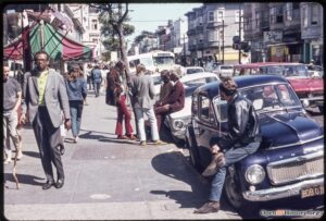 Psychedelic Sixties: Street people (hippies) gathered on sidewalk and sitting on cars in San Francisco in 1969