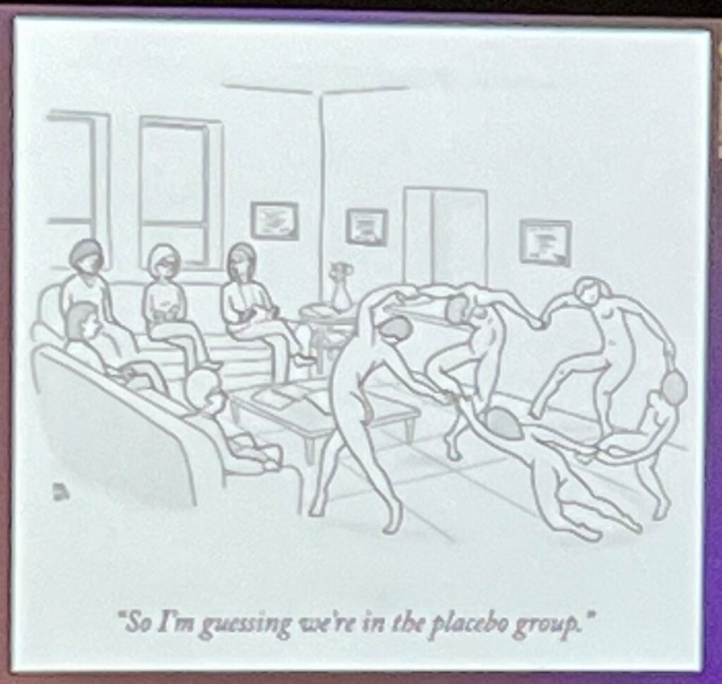 A comic shows two groups of people. On the left the group is seated in a medical waiting room. On the right is a group of nude people dancing in a circle. Someone in the group on the left is saying "So I'm guessing we're in the placebo group."